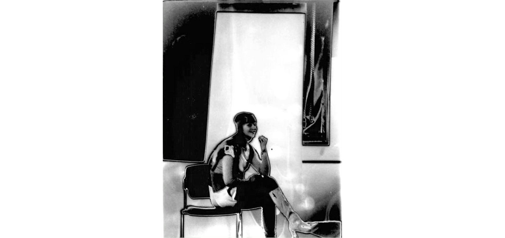 A solarized image of a young woman sitting on a chair. Her body is turned to the side but she smiles at the camera.