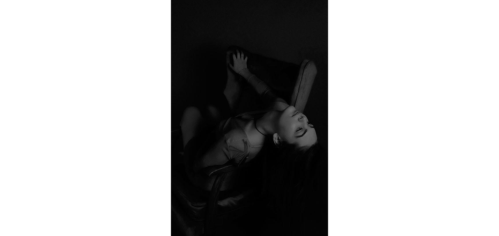 A woman leans backwards over the arm of a chair, her hair falling behind her
