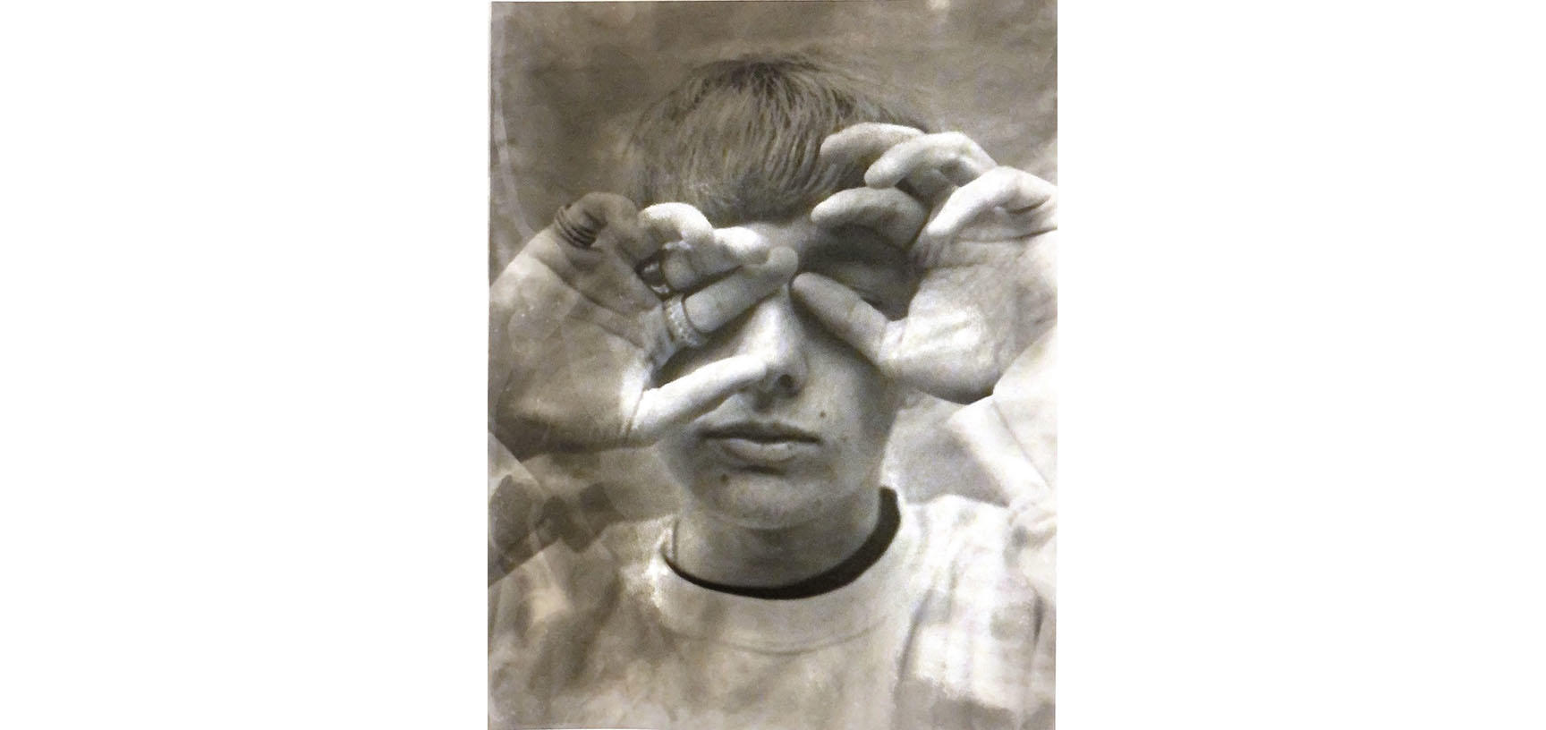 A sepia image of a person. Their head faces the camera but their eyes are covered by their hands - one hand covering an eye, the other makes a circle around the other eye