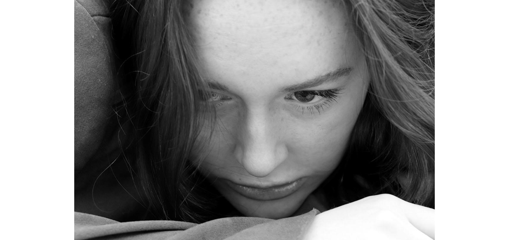 A close up on a woman's face - her eyes are cast down and she rests her chin on her hand